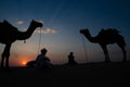 Silhouette of two cameleers and their camels at sand dunes of Thar desert, Rajasthan, India. Cloud with setting sun, sky in the Royalty Free Stock Photo