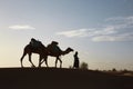 Silhouette of two camels and a cameleer walking in the desert under the beautiful cloudy sky