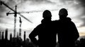 Silhouette of two construction workers watching a building site at sunset symbolizing teamwork dedication and the hard work Royalty Free Stock Photo