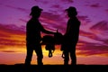 Silhouette of two cowboys holding a saddle in the sunset