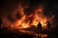 Silhouette of two firemen fighting a raging fire with huge flames of burning scrap