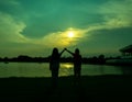Silhouette of two girls holding hands and raised, glad, in front is a lake, a pond, in a park, in the evening, sunset. Royalty Free Stock Photo