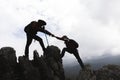 Silhouette of Two male hikers climbing up mountain cliff and one of them giving helping hand. People helping and, team work