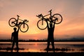 Silhouette two man stand in action lifting bicycle above his head Royalty Free Stock Photo