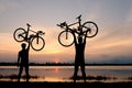 Silhouette two man stand in action lifting bicycle above his head on sunset Royalty Free Stock Photo