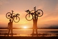 Silhouette two man stand in action lifting bicycle above his head on sunset Royalty Free Stock Photo