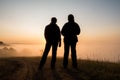 Silhouette of two peple looking at sunrise on foggy valley