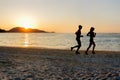 Silhouette of two sportive runners running on the beach at sunset.