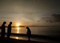 Silhouette of two tourists looking at fisherman searching for shells on the beach during sunrise in Phuket