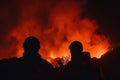 Silhouette of two volcanic scientists with their backs turned observing a volcanic eruption at night with the environment