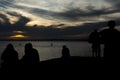 Silhouette of unidentified people enjoying dramatic sunset with dark clouds and sun in yellow color Royalty Free Stock Photo