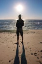 Silhouette of unknown man standing on beach. Loneliness and solitude concept. Men silhouette on sea and clear blue sky background.