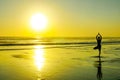 Silhouette of unknown unrecognizable woman standing on beach sea water practicing yoga and meditation looking to the sun on the ho