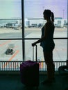 SILHOUETTE: Unknown young woman standing by the window and looking at airport