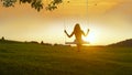 SILHOUETTE: Unrecognizable girl swinging on a tree swing at golden summer sunset