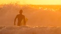 SILHOUETTE: Unrecognizable surfer going surfing on a stunning golden morning. Royalty Free Stock Photo