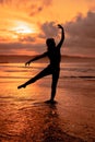 silhouette of a very slender ballerina doing ballet practice alone on the seashore with waves crashing at her Royalty Free Stock Photo