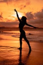 silhouette of a very slender ballerina doing ballet practice alone on the seashore with waves crashing at her Royalty Free Stock Photo