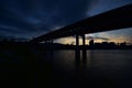 Silhouette view of under a bridge over water with dark buildings on the other side at night Royalty Free Stock Photo