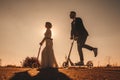 Silhouette wedding couple riding a on scooters along the road outside the city at sunset. Royalty Free Stock Photo