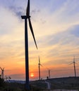 Silhouette wind turbine farm over moutain with orange sunset and Royalty Free Stock Photo