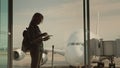 A silhouette of a woman with boarding documents in hand, awaiting landing on her flight. Stands at the window in the