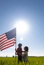 silhouette woman and child, mother son in green field look at each other, hold American flag in backlight of bright sun Royalty Free Stock Photo