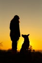 Silhouette woman with a dog looking at each othe rin the field at sunset, pet sitting near girl`s leg on nature,concept of Royalty Free Stock Photo