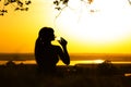 Silhouette of a woman drinking water after physical exercise in nature, girl profile at sunset, concept of sport and relaxation Royalty Free Stock Photo