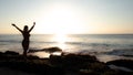 Excited young woman raising arms at the beach in front of the ocean. View from back. Sunset at the beach. Bali, Indonesia Royalty Free Stock Photo