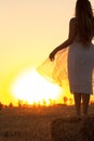 Silhouette woman figure at sunset standing on hay stack, beautiful romantic girl with long hair posing outdoors in field