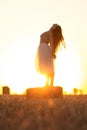 Silhouette woman figure at sunset standing on hay stack, beautiful romantic girl posing outdoors in field, freedom concept Royalty Free Stock Photo