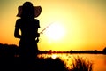 Silhouette of a woman with a fishing rod on the nature at dawn Royalty Free Stock Photo