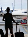 SILHOUETTE: Woman grabs her luggage and looks through the window at airplane. Royalty Free Stock Photo