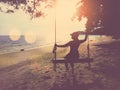 Silhouette woman with hat sitting on wooden swing at sunset beach background Royalty Free Stock Photo