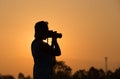 Silhouette of a woman holding camera taking pictures outside during sunrise or sunset Royalty Free Stock Photo