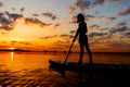 silhouette of woman on inflatable SUP board and paddling through shining water surface