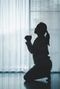 silhouette of woman kneeling and praying in modern church at sunset time. Female catholic prayer worship to God wish a better life Royalty Free Stock Photo