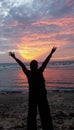 Silhouette of a woman looking at the open sea with a golden sunset sky in the shape of a triangle from the edge of a beach. Royalty Free Stock Photo