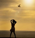 Silhouette of a woman looking out at a helicopter  flying over the ocean Royalty Free Stock Photo