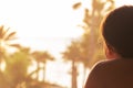 Silhouette of woman lying on the sunbed on terrace and looking on palm trees sea beach at sunset. Female relaxing. Back view.