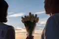 Silhouette of woman and man holding in their hands a bouquet of white tulips flowers against sunset beach. Royalty Free Stock Photo