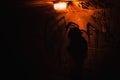A silhouette of a woman passing in a dark red rusty tunnel with dim orange lights