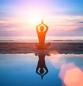 Silhouette of a woman practicing yoga on the beach with reflection in water. Royalty Free Stock Photo