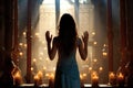 Silhouette of a woman in prayer, with raised hands, illuminated by radiant light from candles