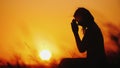 Silhouette of a woman praying against the background of an orange sky and a large setting sun Royalty Free Stock Photo