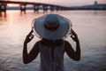 The silhouette of a woman by the river at sunset. Rear view of the silhouette of a woman in a straw hat enjoying the Royalty Free Stock Photo