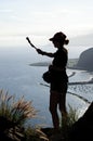 Silhouette of a woman shooting with a selfie stick against the backdrop of a beautiful seascape.