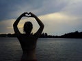 Silhouette of a woman showing heart sign in front of a lake in summer