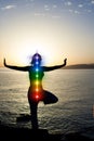 Silhouette of woman sits in a Upward Salute pose on beach sunset view, glowing seven all chakra. Kundalini energy. girl practicing Royalty Free Stock Photo